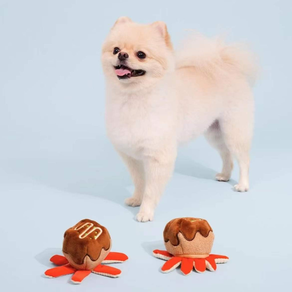 Small white dog standing next to two plush takoyaki toys, shown for size