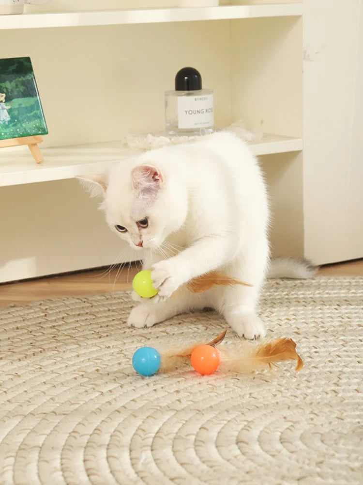 White cat playing with feather bouncer balls on a rug